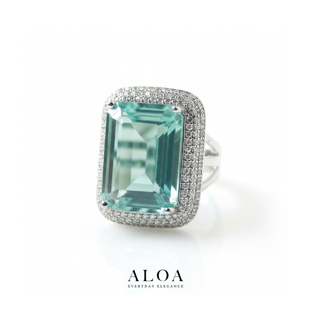 Ring with a large green gemstone and diamond-studded band on a white background, featuring the brand 'ALOA'.