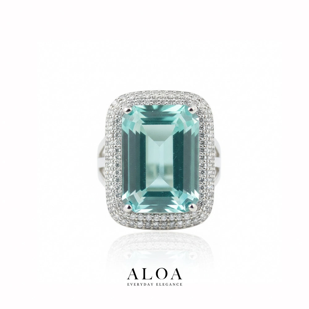 Ring with a large green gemstone and diamond-studded band on a white background, featuring the brand 'ALOA'.